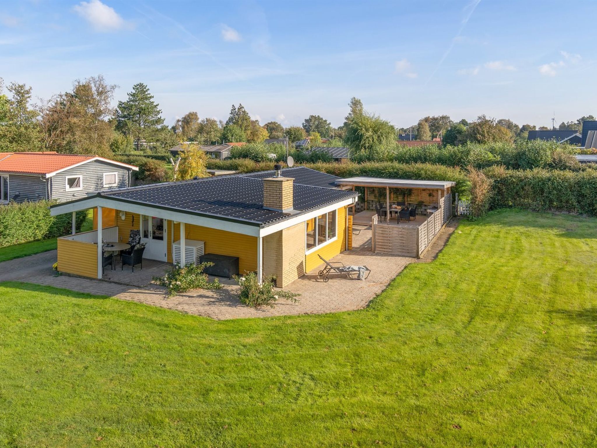 A modern house with a covered patio, a small garden, and a neighboring house.