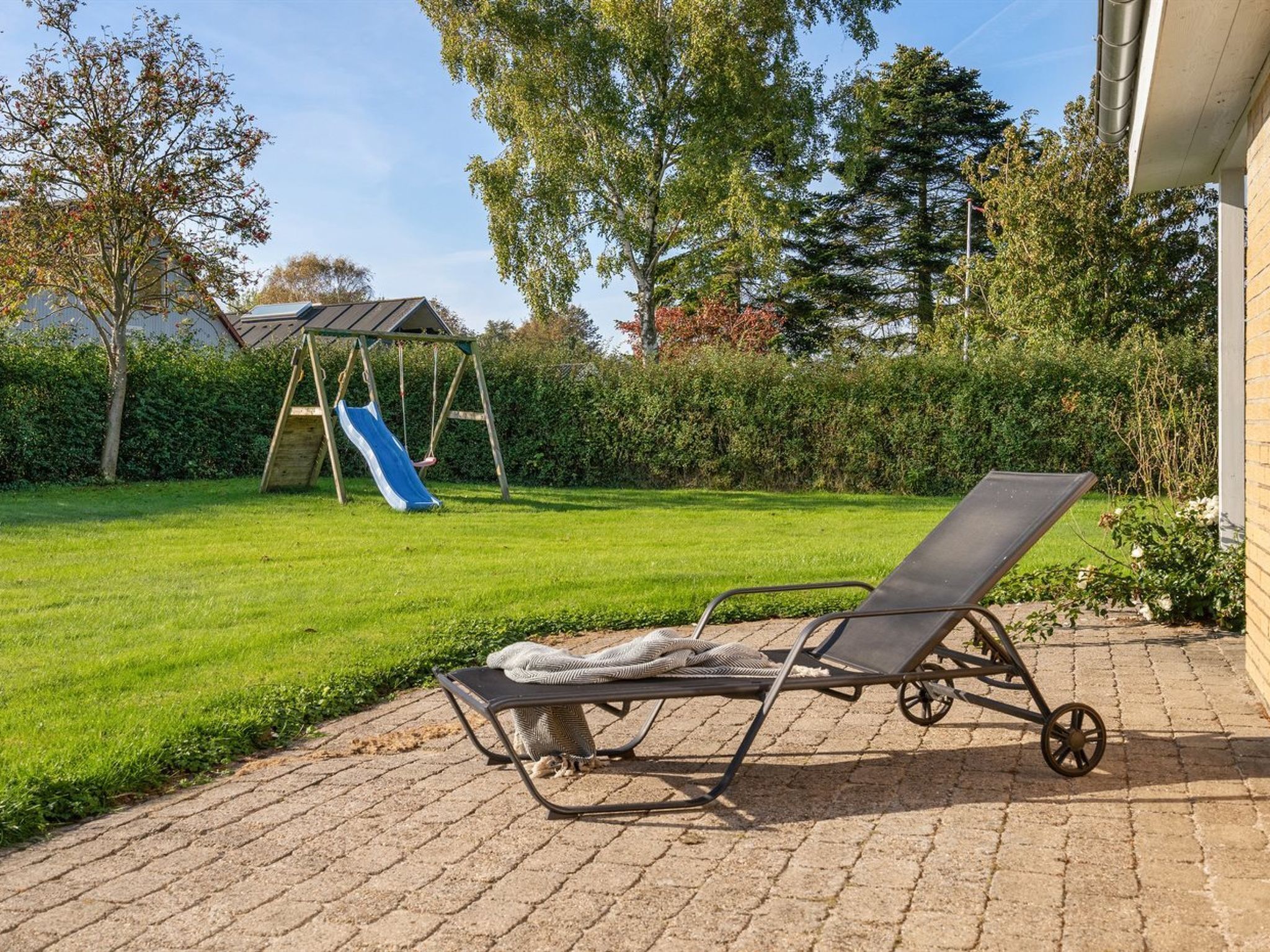 A patio with a sun lounger and a swing set in a backyard.