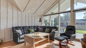 Un salon moderne avec un canapé d’angle en cuir noir, une table basse en bois et un fauteuil noir. De grandes fenêtres offrent une vue sur l’extérieur.