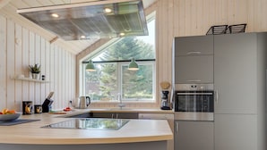 Une cuisine moderne dotée d’un grand îlot central, d’appareils électroménagers en acier inoxydable et d’une fenêtre offrant une vue sur les arbres.