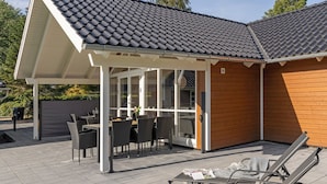 Une terrasse couverte, aménagée avec du mobilier d’extérieur, un coin repas et un mur en bois.