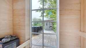Une chambre moderne dotée d’une grande fenêtre, d’un jacuzzi et d’une terrasse en bois visible de l’extérieur.