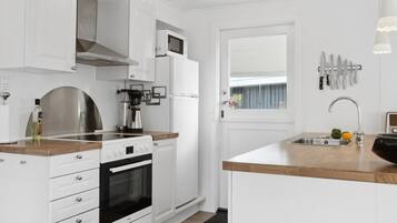 Une cuisine moderne avec des meubles blancs, un four encastré, une machine à café et un évier placé sous une fenêtre.