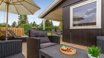 Un patio abrité, aménagé avec des meubles en osier, une table sur laquelle est posé un panier de fruits et un grand parasol.
