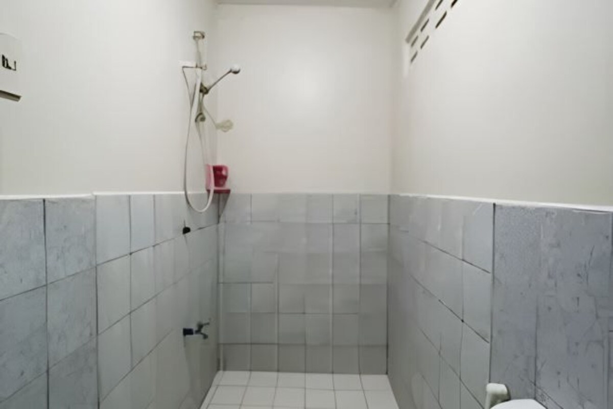 A small, enclosed shower area with tiled walls and floor, a handheld showerhead, and a red soap dispenser.