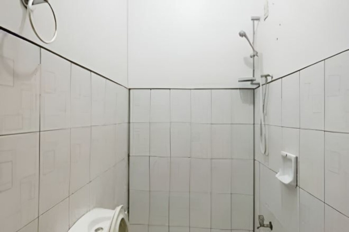 A small, white-tiled bathroom with a toilet, a shower, and a hand dryer.