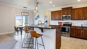 A modern kitchen with a central island, bar stools, wooden cabinets, stainless steel appliances, and pendant lighting. - Conveniently located Clean Rambler. (Kennewick)