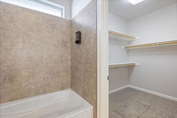 A bathroom with a bathtub, a shower, and a toilet. There are shelves on the wall.