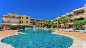A hotel with a central swimming pool, multiple balconies, and a clear blue sky.