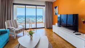 A living room with a TV, sofa, and a view of the ocean.
