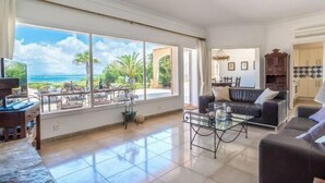 A spacious living room with a large window overlooking a tropical landscape, a comfortable sofa, a coffee table, and a television. - Las Gaviotas Style & Charm by Interhome (Ses Salines)