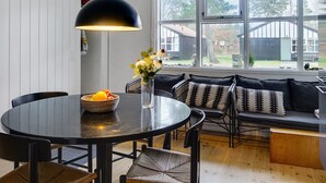 Una cocina moderna con una mesa de comedor redonda, sillas negras, una lámpara colgante negra y un ventanal con vista al jardín trasero.