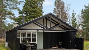 Una casa moderna con fachada negra, terraza de madera y un ventanal grande.