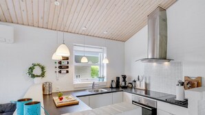 Moderni keittiö, jossa on valkoiset kaapit, ruostumattomasta teräksestä valmistettu liesituuletin ja ikkuna, josta avautuu näkymä vehreään maisemaan.