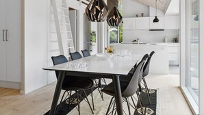 A modern kitchen with white cabinets, a dining table with chairs, and pendant lights. - "Elin" - 200m from the sea by Interhome (Idestrup)