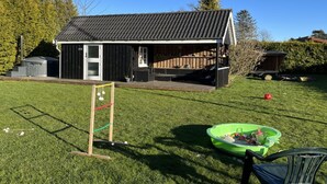 A small building with a dark roof and a wooden deck, surrounded by a grassy yard and trees. - "Annegret" - 250m from the sea by Interhome (Idestrup)