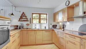 A kitchen with wooden cabinets, a stove, a microwave, and a window with a view of greenery. - "Annegret" - 250m from the sea by Interhome (Idestrup)