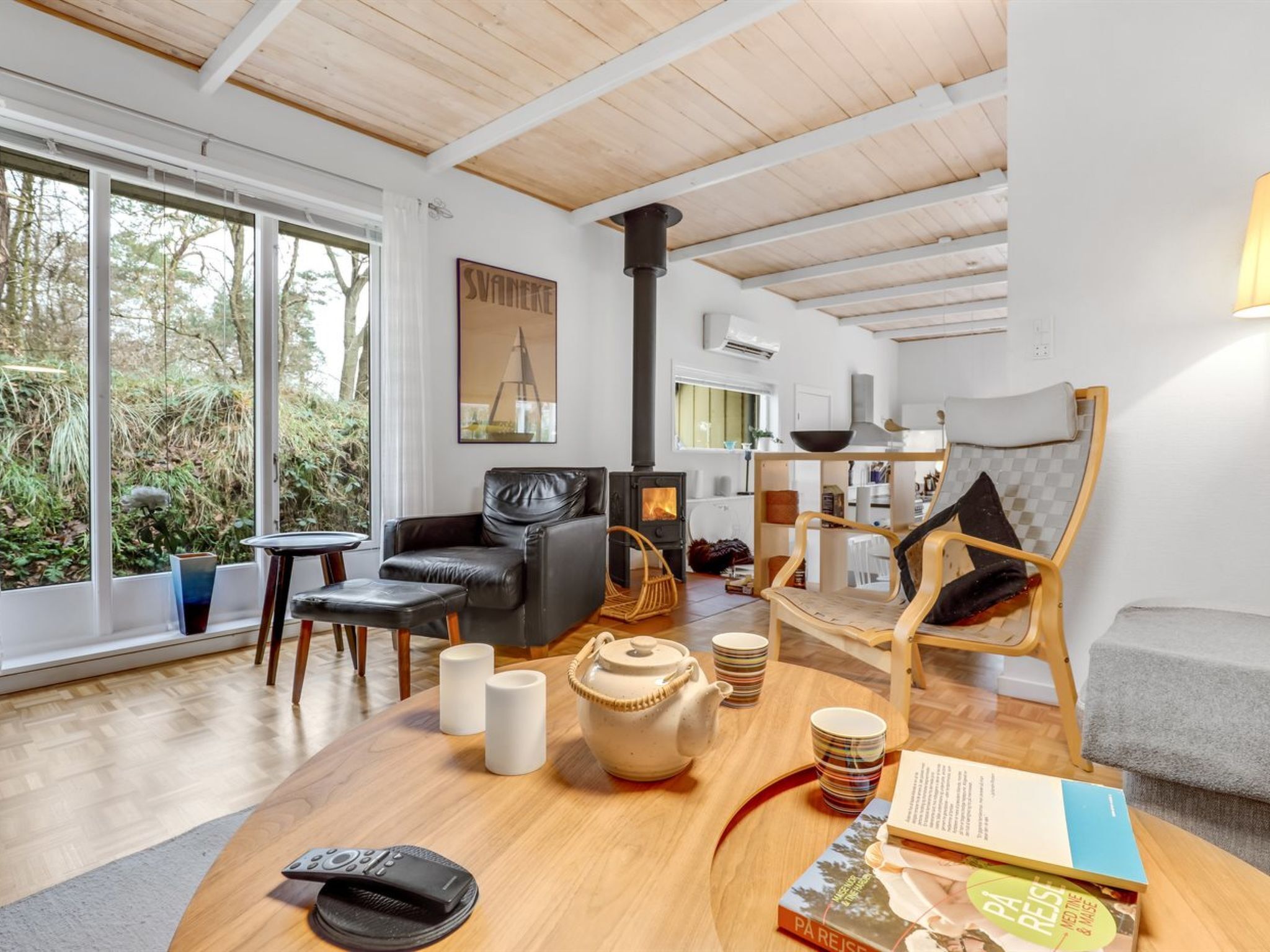 A modern living room with a fireplace, a sofa, a coffee table with books and cups, and a view of the outdoors.