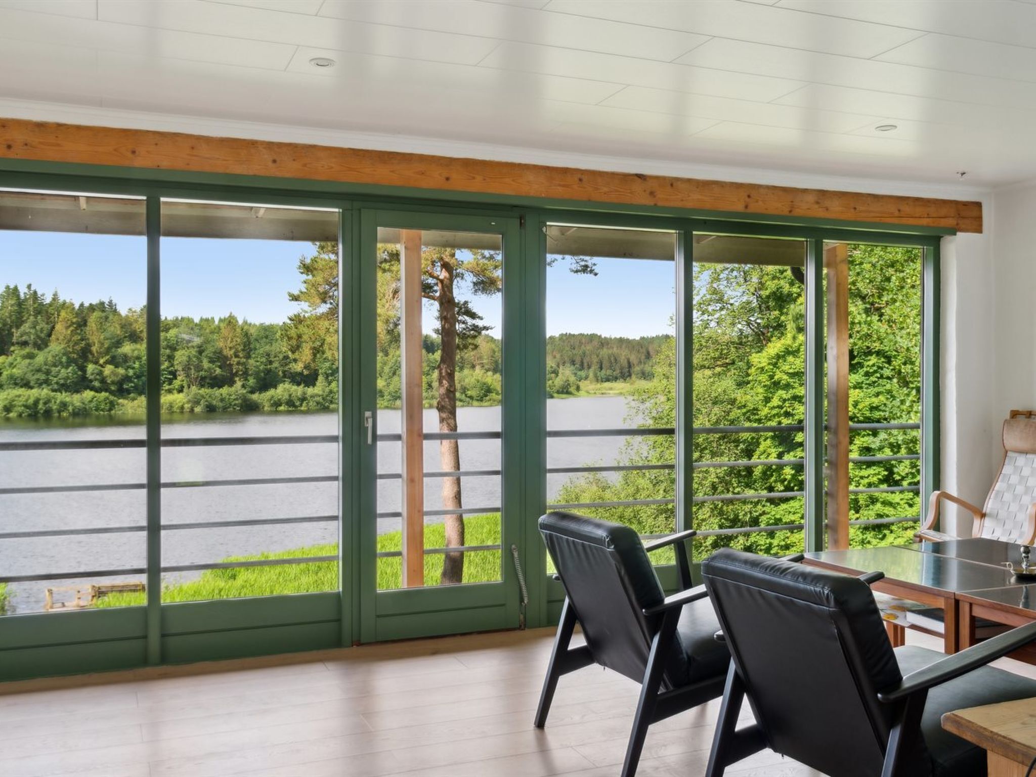 Habitación con amplios ventanales con vistas a un lago, amueblada con sillas y una mesa.