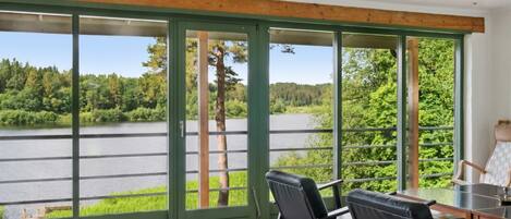 Habitación con amplios ventanales con vistas a un lago, amueblada con sillas y una mesa.
