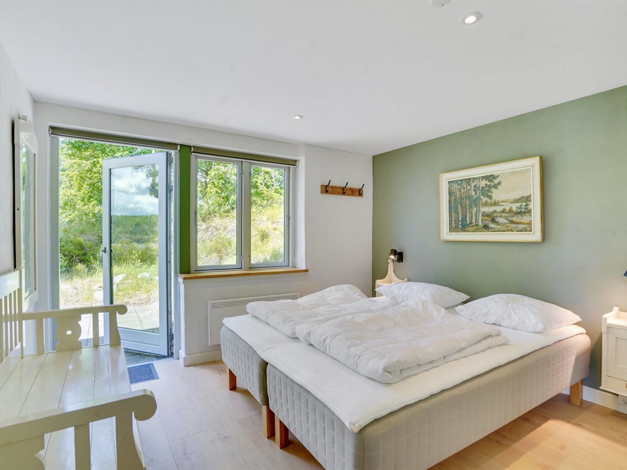 A bedroom with two beds, a window, a painting, and a desk.