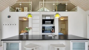 A modern kitchen with a black countertop, two white bar stools, and pendant lights.