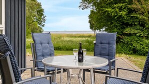 A round glass table with four blue checkered chairs, a bottle of wine, and two wine glasses.