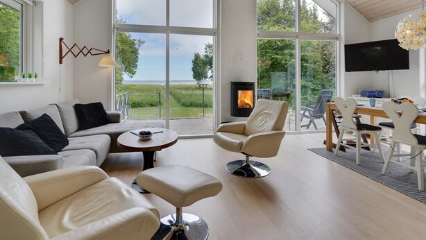 A spacious living room with a large window, a fireplace, and a dining area with white furniture.
