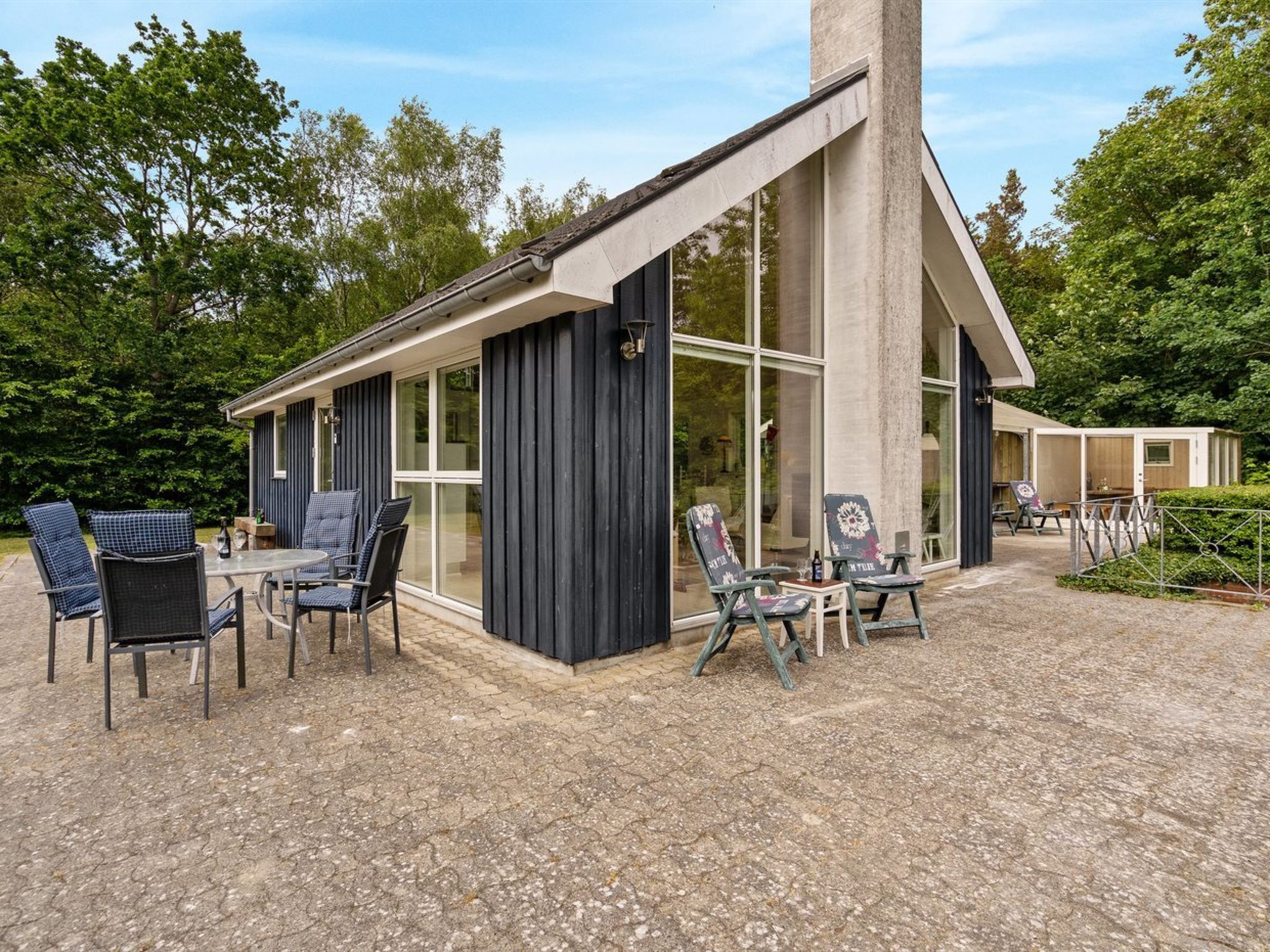 Une cabane moderne dotée d’une grande baie vitrée, d’un coin repas avec des sièges extérieurs et d’une terrasse en gravier.