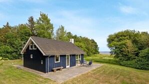 A small, dark blue cabin with a sloped roof, a patio with outdoor seating, and a view of the sea.