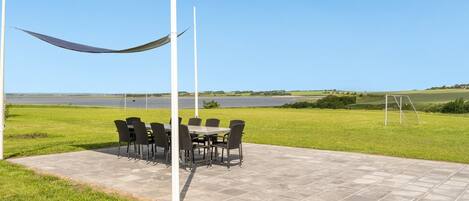 An outdoor patio with a table and chairs, a hammock, and a view of a lake and fields.