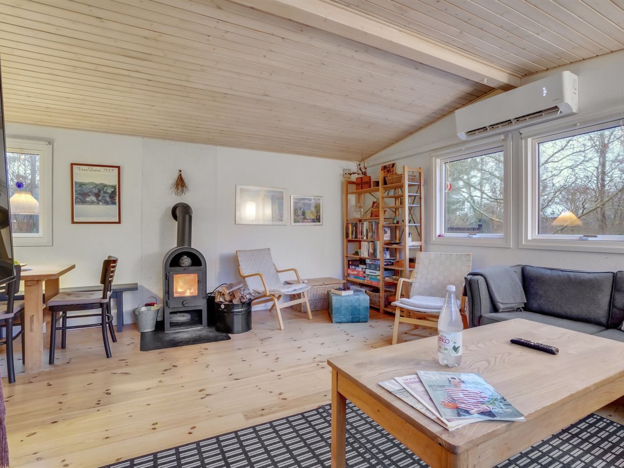 Ein gemütliches Wohnzimmer mit Kamin, Holzmöbeln, einem Bücherregal und großen Fenstern.