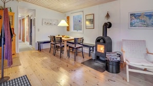 A cozy room with a wooden ceiling, a dining table with chairs, a wood-burning stove, and a painting on the wall.