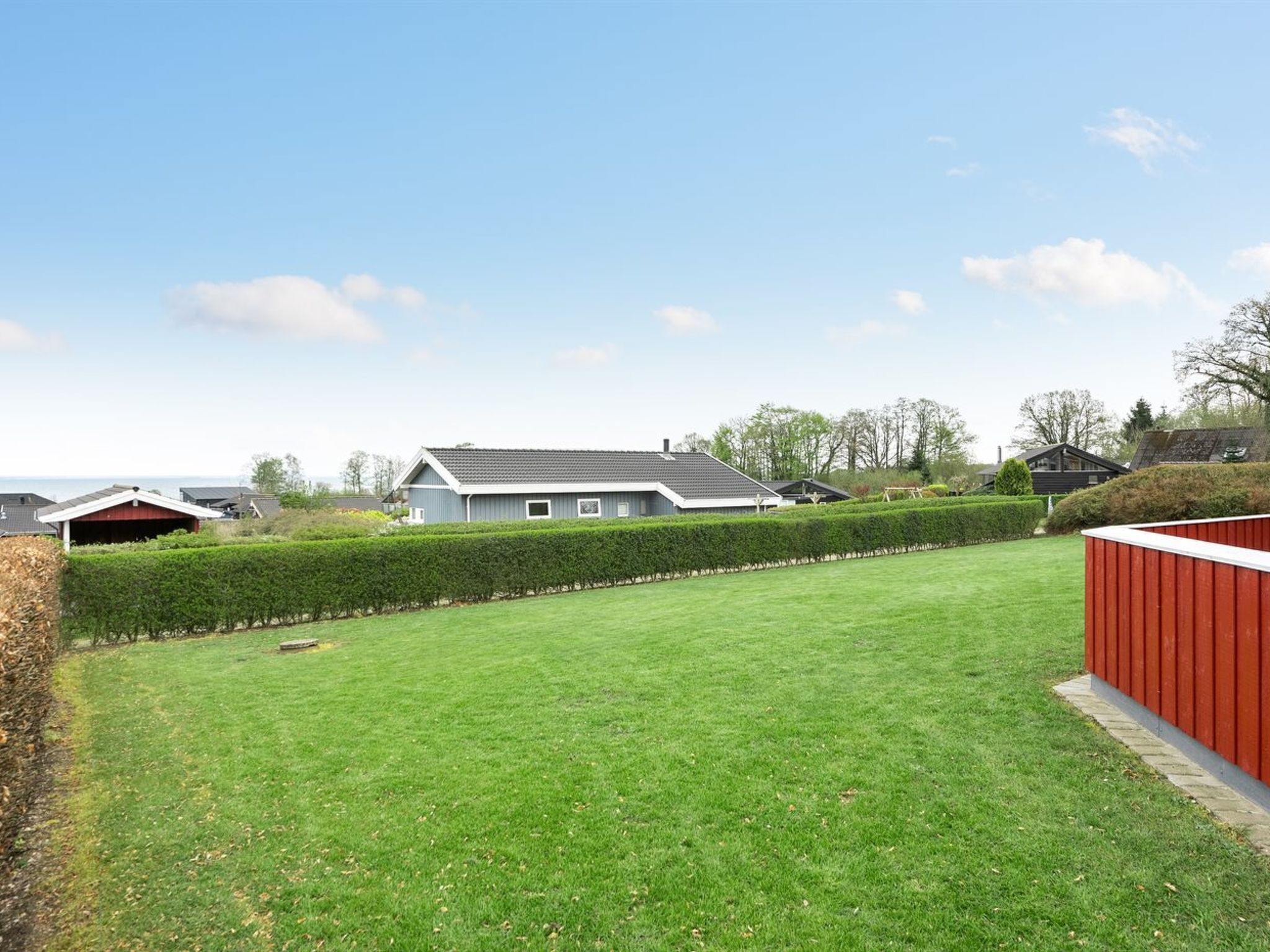 Een woonhuis met een verzorgd gazon, een rode schuur en een woning met een grijs dak.