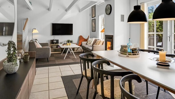 Een moderne woonkamer met een open haard, een eetgedeelte met een grote tafel, en een keuken met een bar.