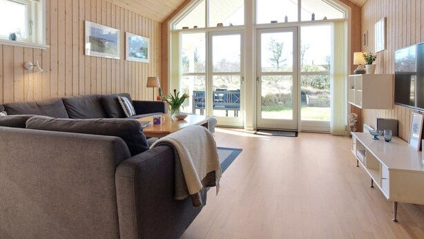 Un salon spacieux avec un plafond haut, des murs en bois, une grande fenêtre et un meuble moderne pour la télévision.