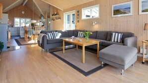 Un vaste espace de vie doté d’un plafond en bois, d’un canapé gris, d’une table basse en bois et d’un coin repas avec une table et des chaises.