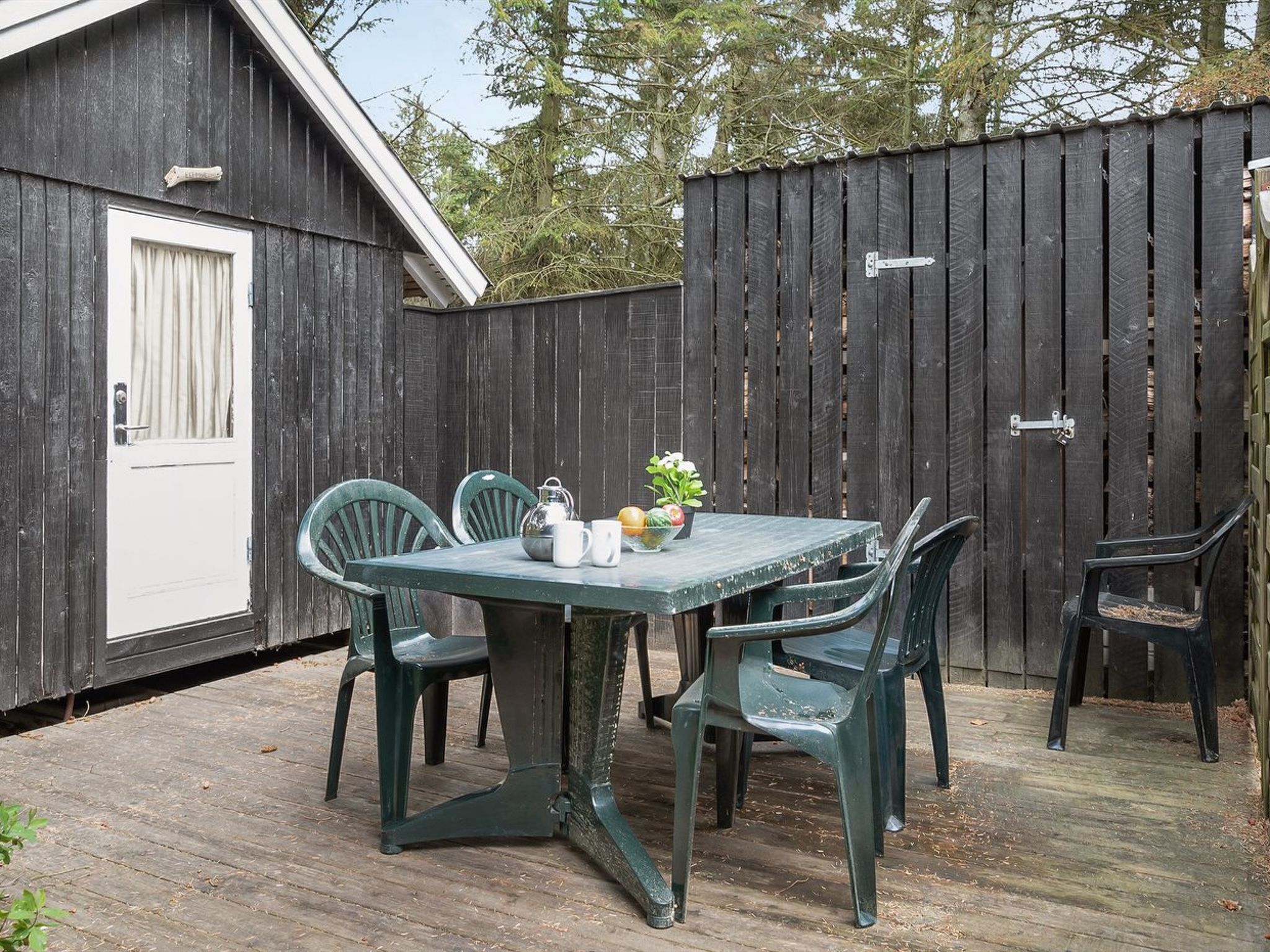 Un patio in legno con tavolo e sedie, una porta e una recinzione.