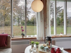 Une pièce chaleureuse avec une grande fenêtre, une table ornée de théières et de tasses, et une plante en pot.