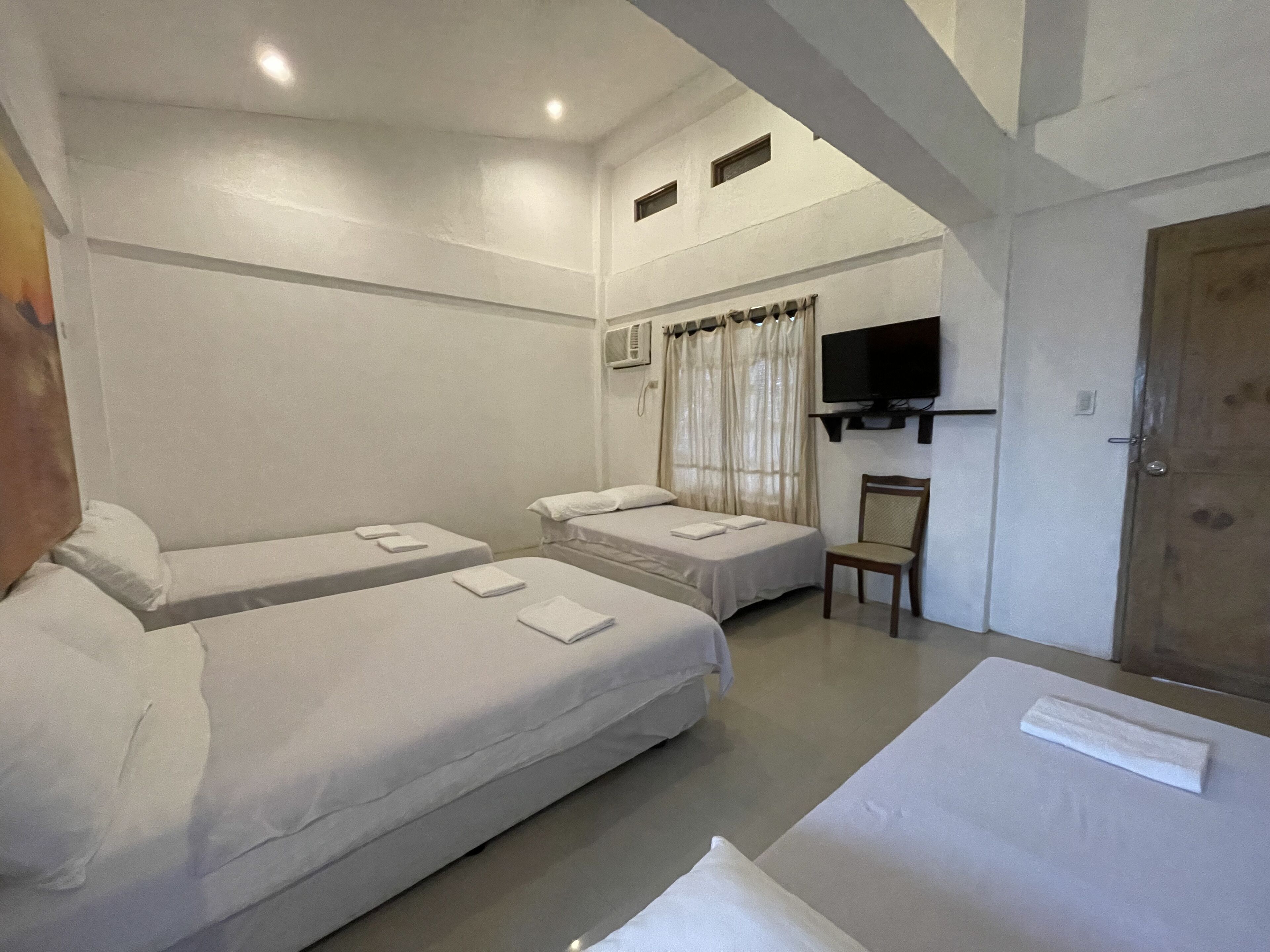 Ein Hotelzimmer mit zwei Einzelbetten, einem Fernseher, einem Sessel und einer Holztür.