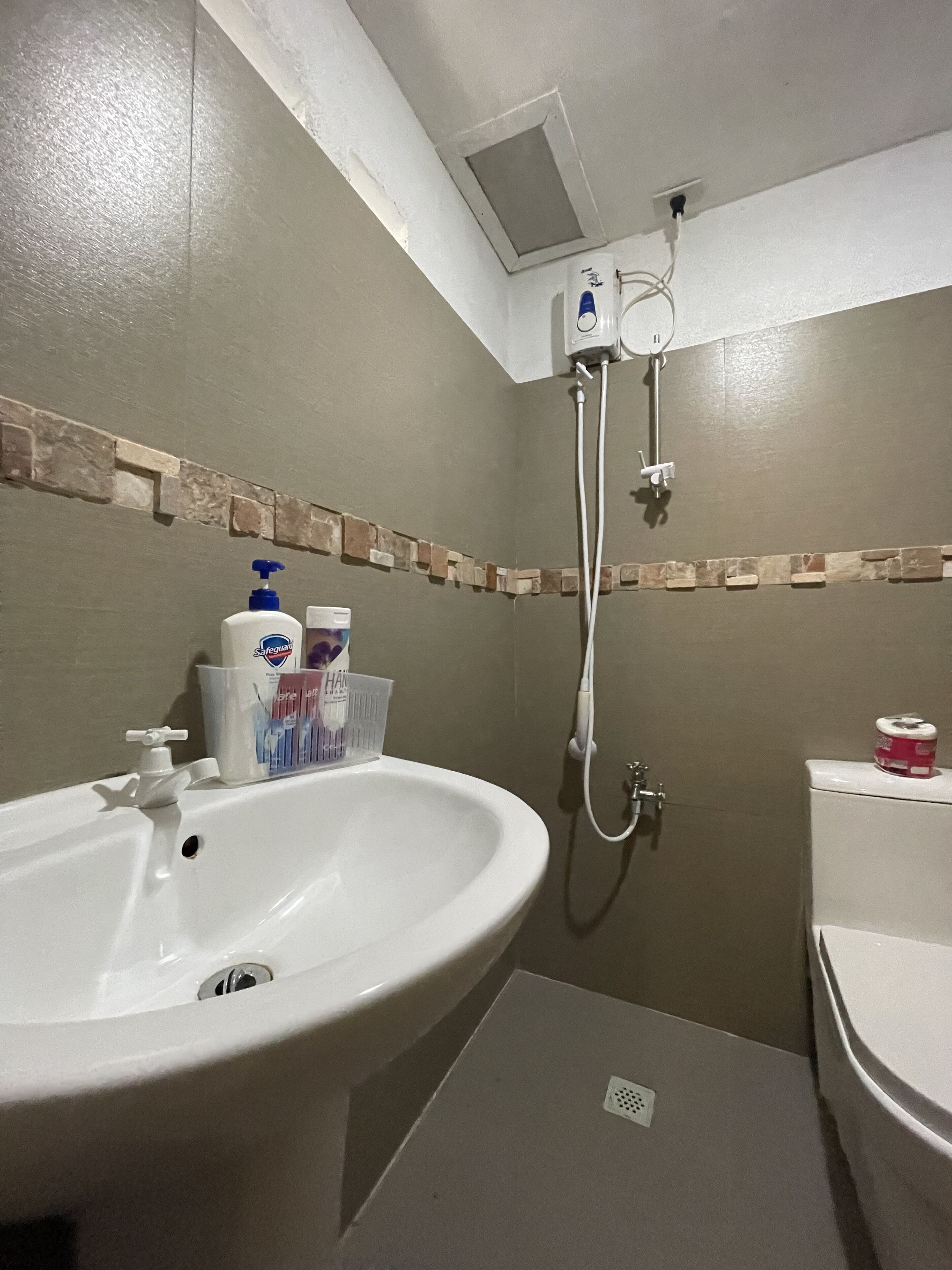 A bathroom with a white sink, a shower, and a toilet. There are toiletries on the sink and a towel rack above the shower.