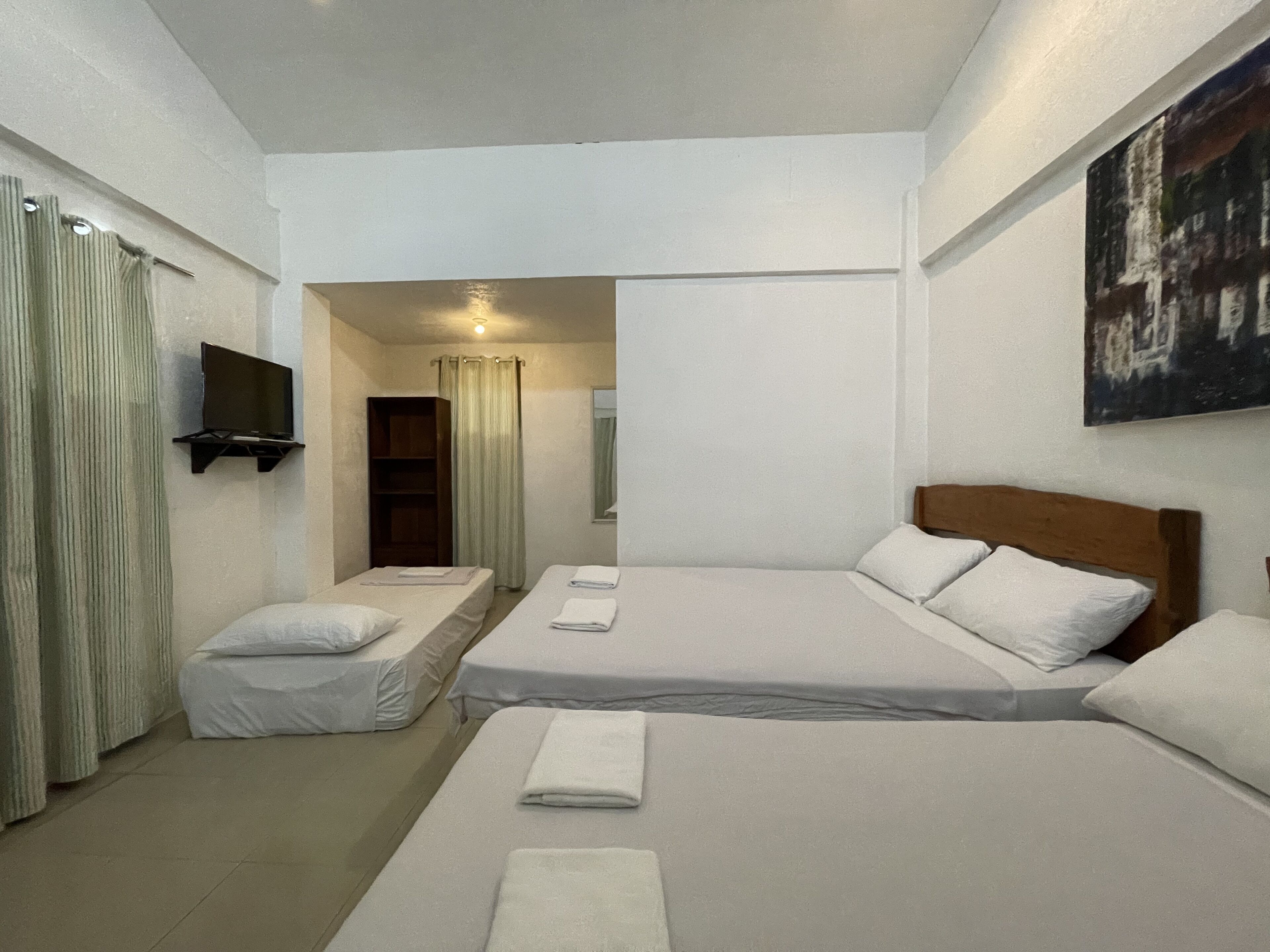 A hotel room with two beds, a TV, a bookshelf, and a painting on the wall.