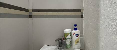 Un baño con un lavamanos blanco, una ventana encima y artículos de aseo sobre el lavamanos.