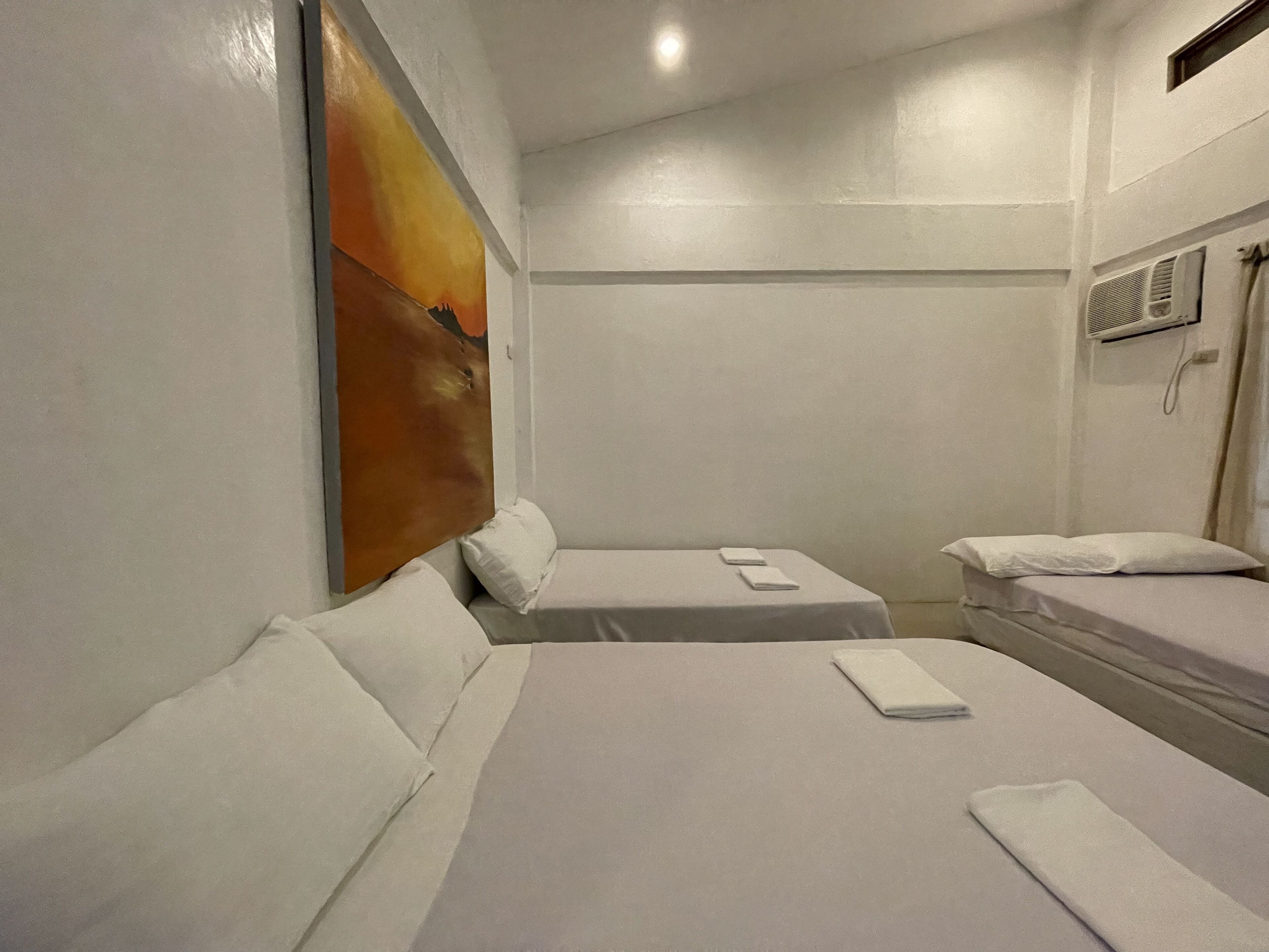 A hotel room with two beds, a painting on the wall, and an air conditioning unit.