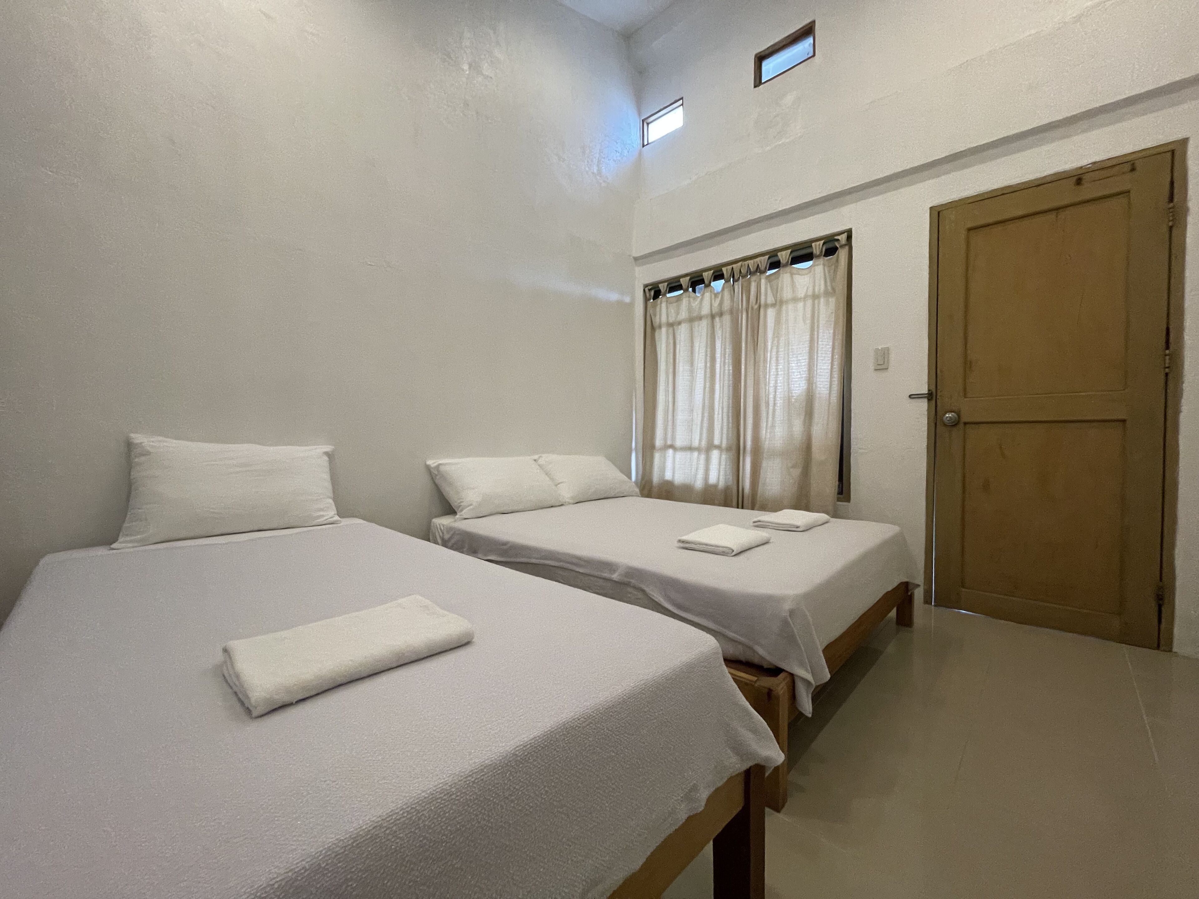 A room with two single beds, a wooden door, and a window with curtains.