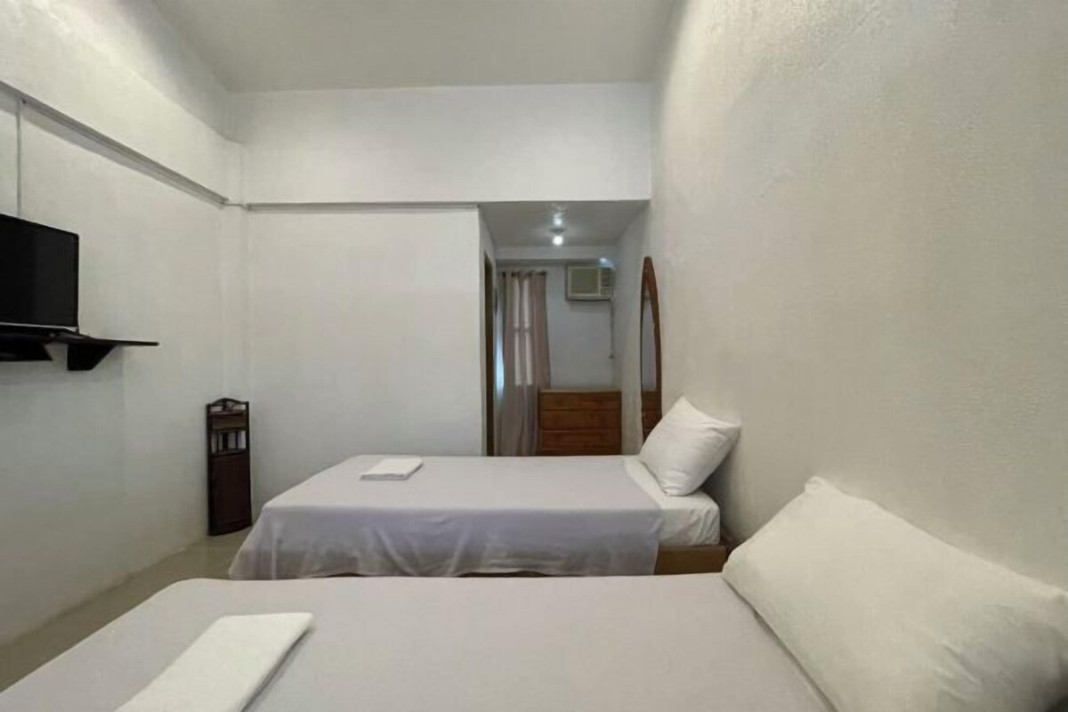 A small, clean room with two beds, a TV, and a mirror.