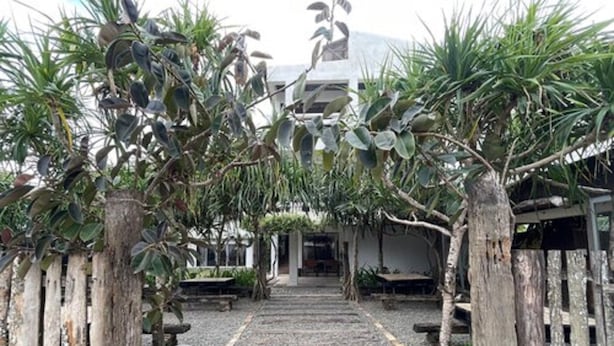 A pathway leading to a building with a wooden fence on either side, surrounded by potted plants. - Akkaw Baler Hometel (Baler)