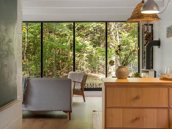 A room with a large window, a wooden dresser, a chair, and a hanging light fixture.