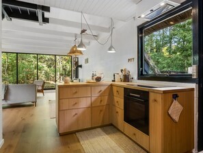 Een moderne keuken met houten kastjes, een zwarte vaatwasser en een groot raam met uitzicht op de omgeving.