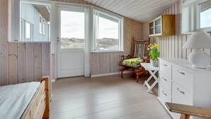 A room with wooden walls and a sloped ceiling, a bed, a chair, a table with a lamp, and a view of the outdoors. - "Kulle" - 200m from the sea by Interhome (Saltum)